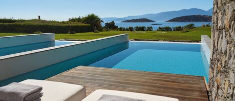 A pool area with two lounge chairs and towels, a wooden deck, and a view of the sea and mountains.