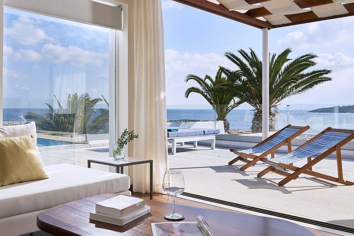 A modern room with a sofa, a table, and a view of the sea and palm trees.