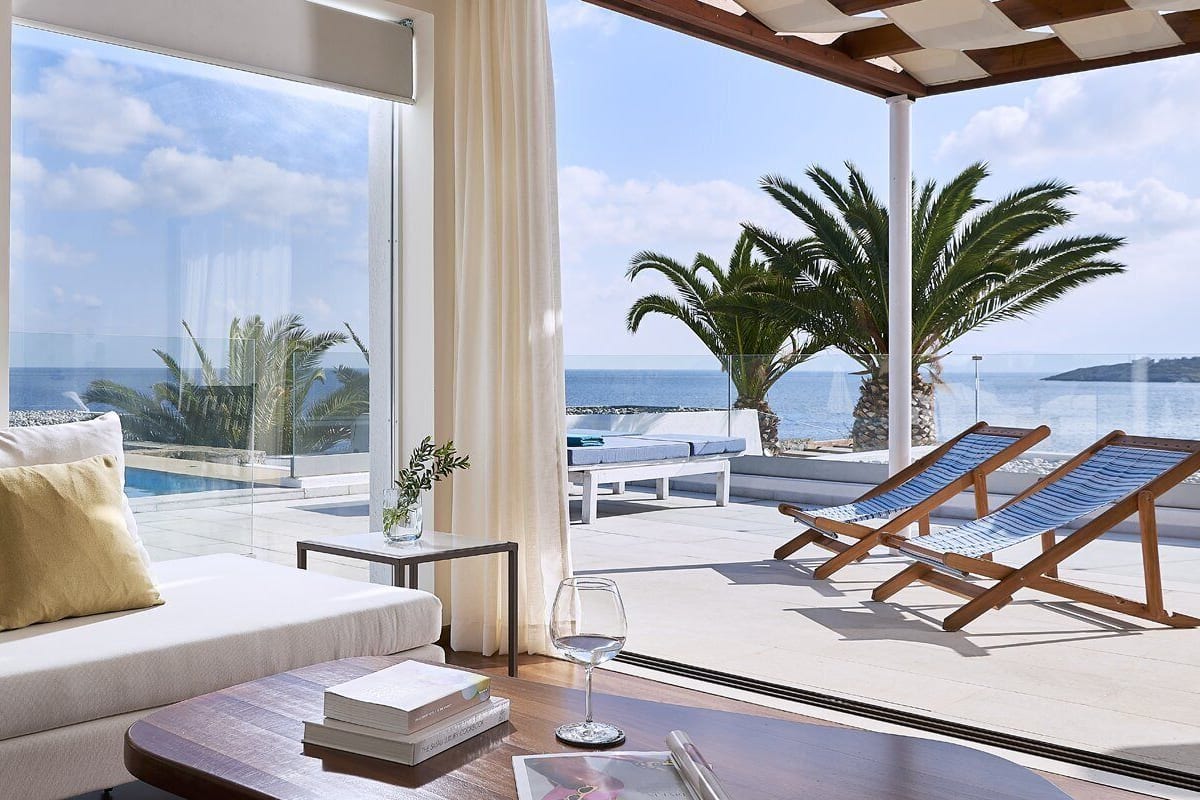 A modern room with a sofa, a table, and a view of the sea and palm trees.