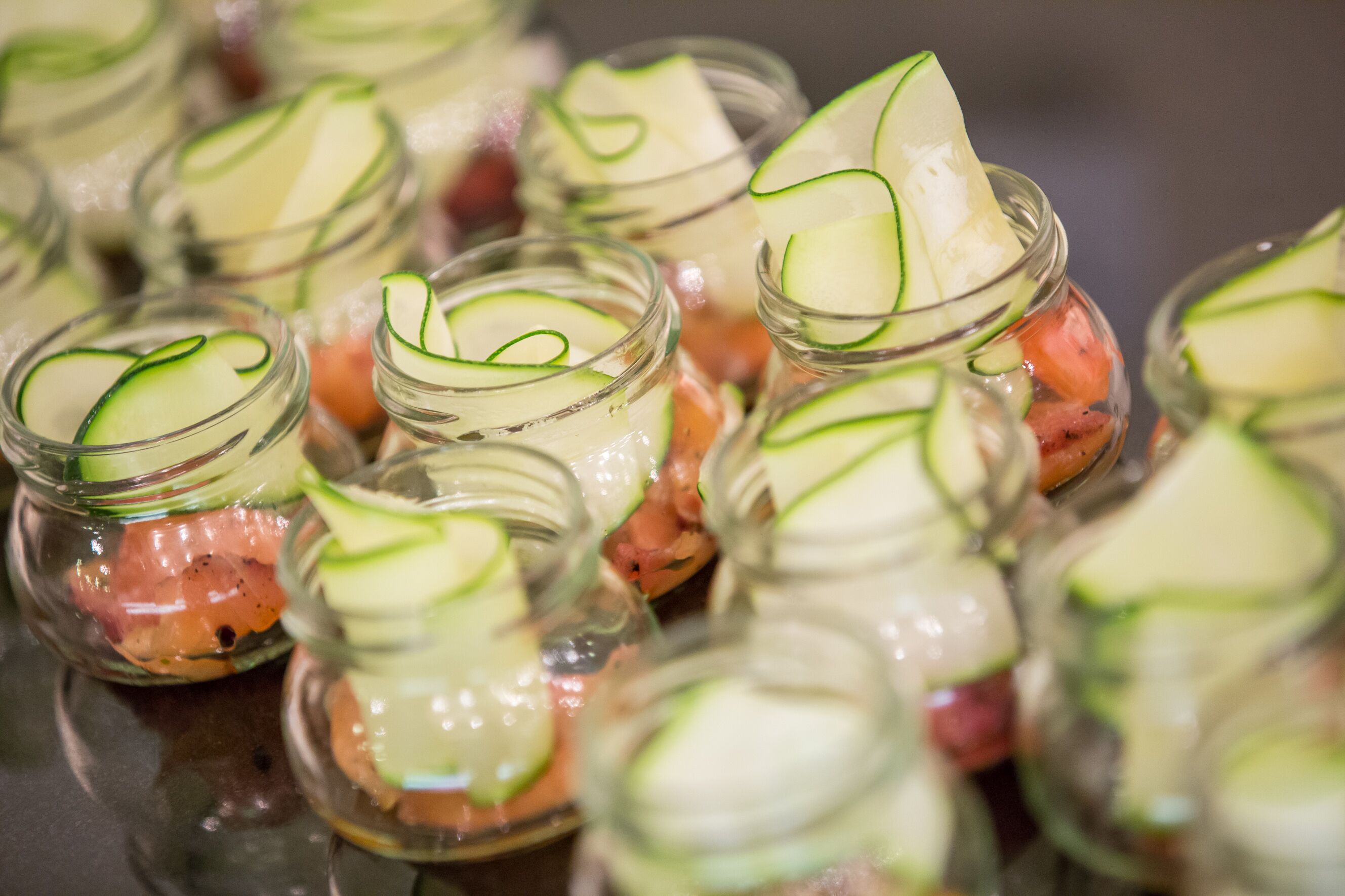 A close-up of several glass jars containing a layered salad with cucumber slices and other ingredients.