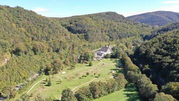 A large, modern building surrounded by lush green hills and a winding path.