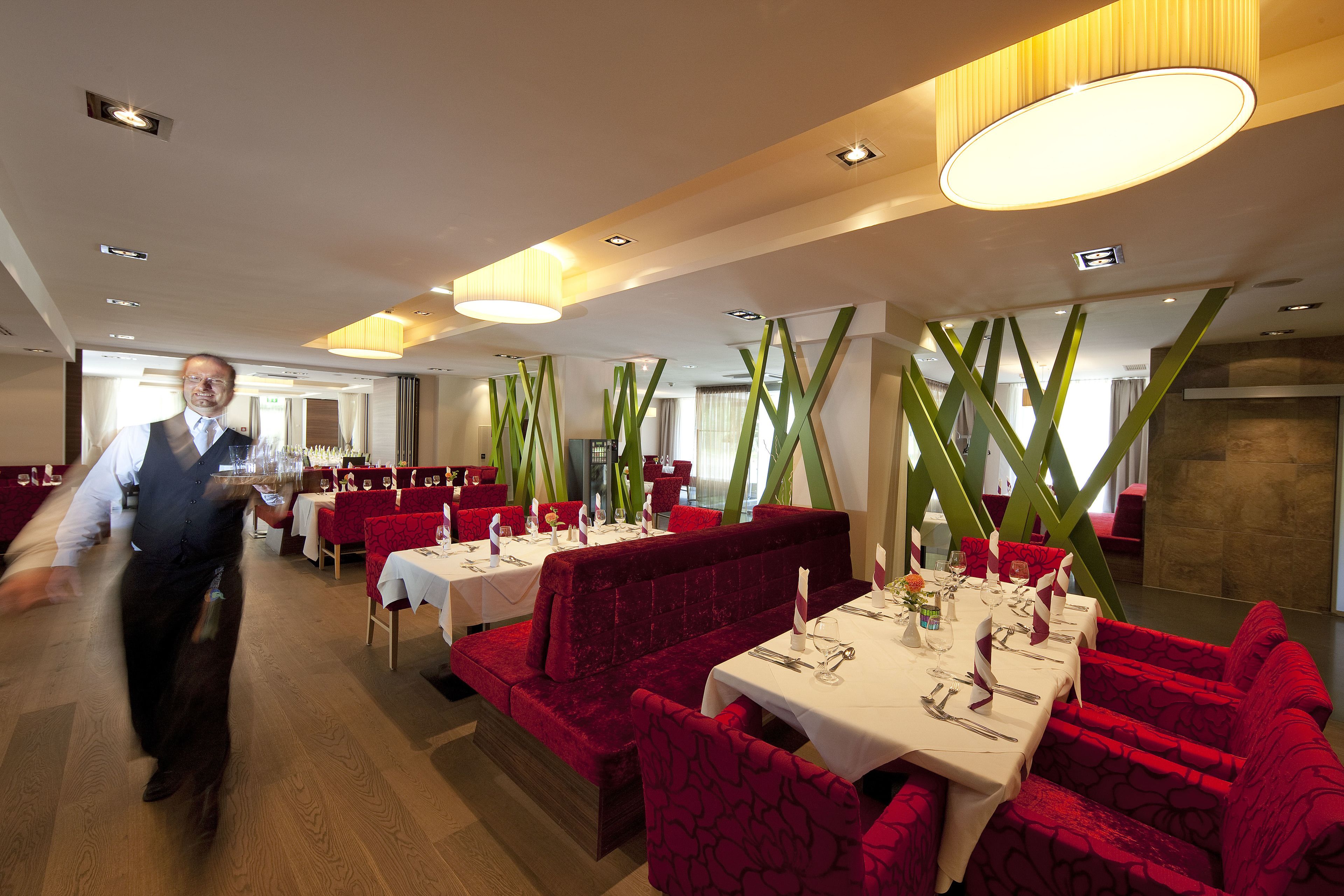 En restaurant med røde polstrede siddepladser, hvide duge og moderne hængelamper.