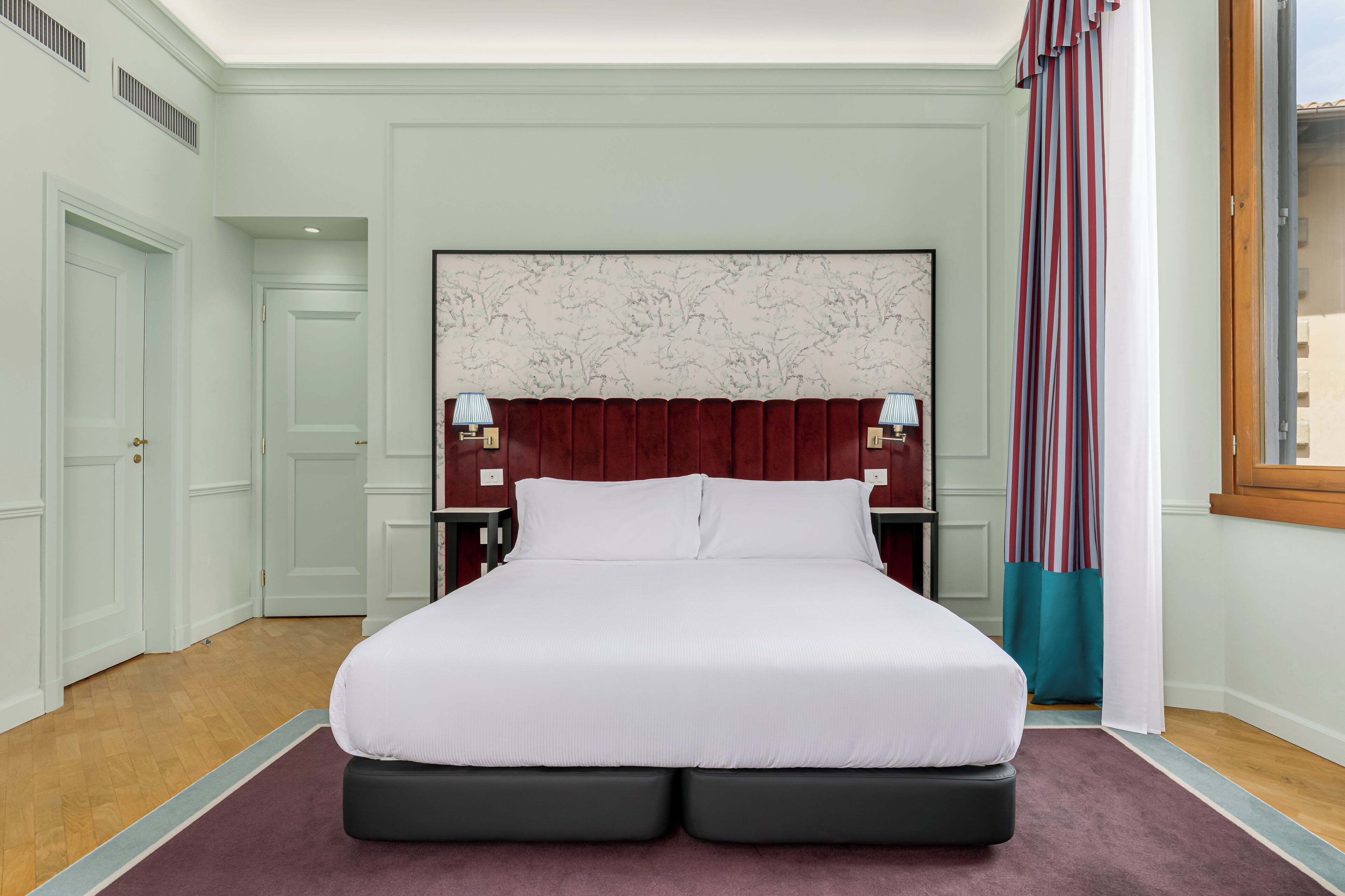 Ein ordentlich eingerichtetes Schlafzimmer mit einem großen Bett, einem Kopfende mit Marmorstruktur und einem Fenster mit Vorhängen.