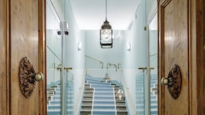 A hallway with wooden doors, a checkered floor, and a staircase with blue steps. - Room Mate Collection Isabella, Florence (Florence)