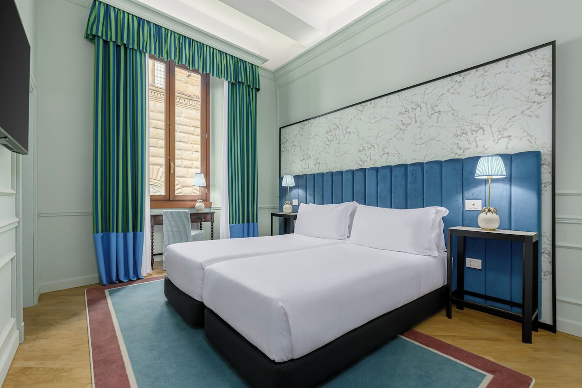 A hotel room with a large bed, two bedside tables, a desk, and a chair.