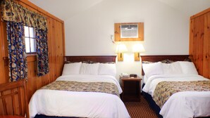 Habitación de hotel con dos camas, cabeceros de madera, una mesita y una ventana con cortinas.