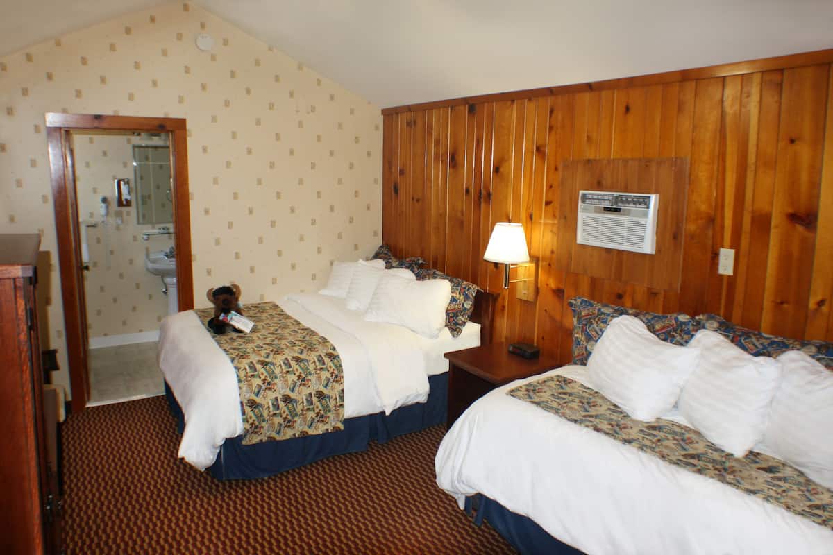 A hotel room with two beds, a wooden wall paneling, a lamp, and a mirror.
