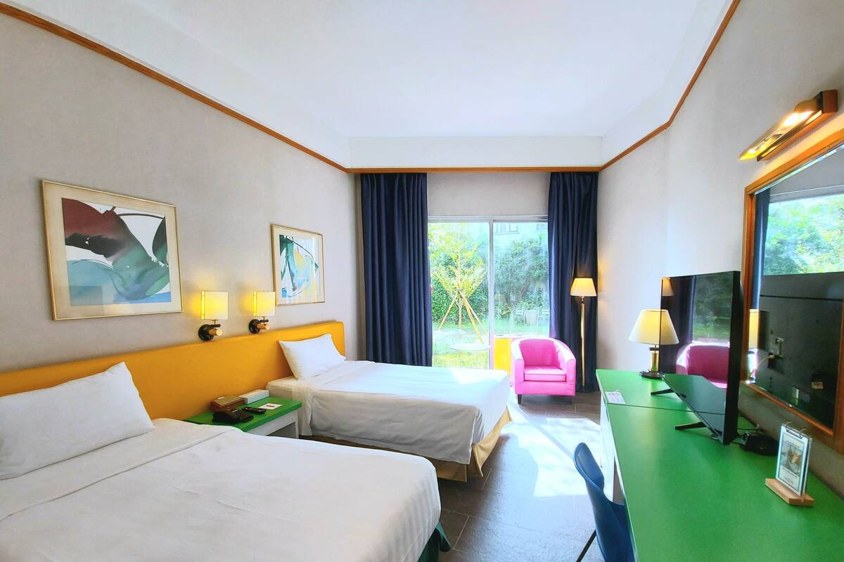 Habitación de hotel con dos camas, un escritorio, una silla, un televisor y una ventana con cortinas.