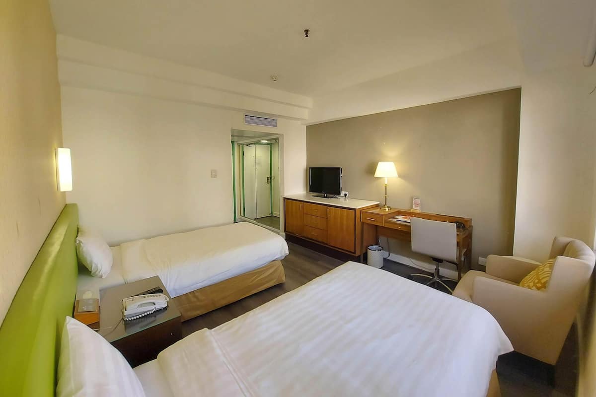 Una habitación de hotel con dos camas, un escritorio con computadora, una silla y un televisor.