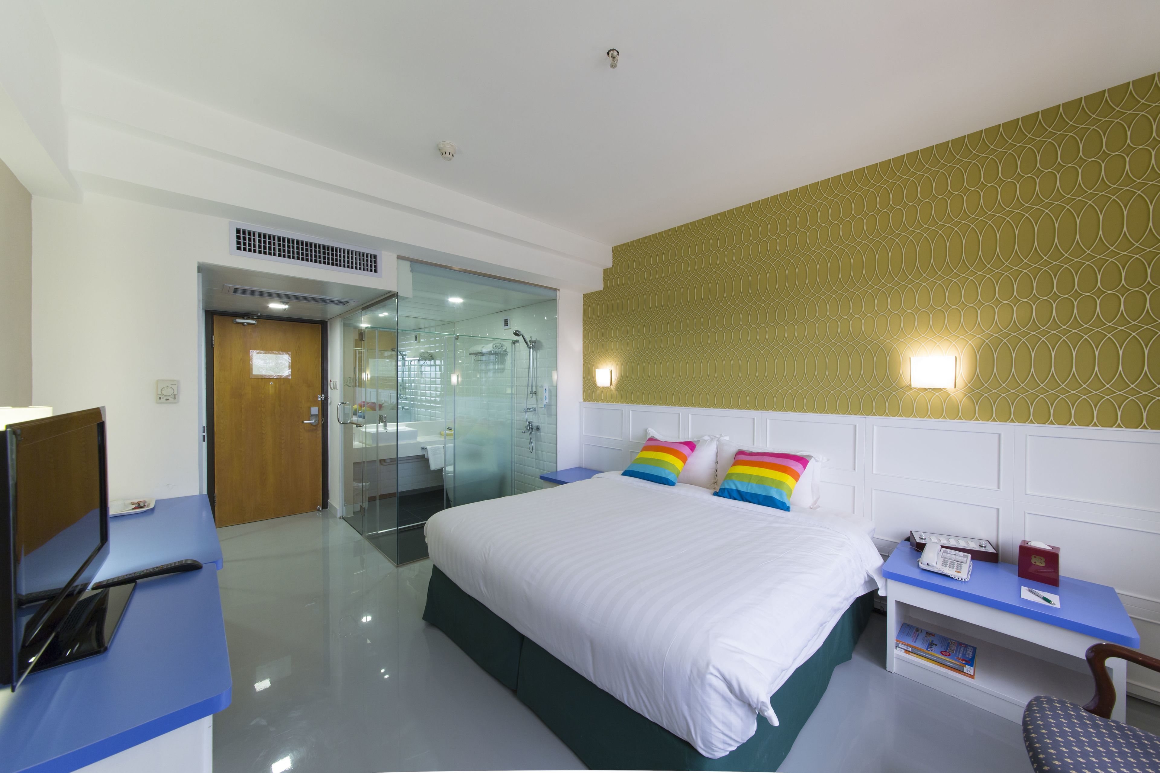 Une chambre d’hôtel comprenant un lit, un bureau avec un ordinateur, une table de chevet avec un téléphone et un livre, ainsi qu’un espace douche.