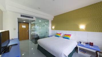 Une chambre d’hôtel comprenant un lit, un bureau avec un ordinateur, une table de chevet avec un téléphone et un livre, ainsi qu’un espace douche.