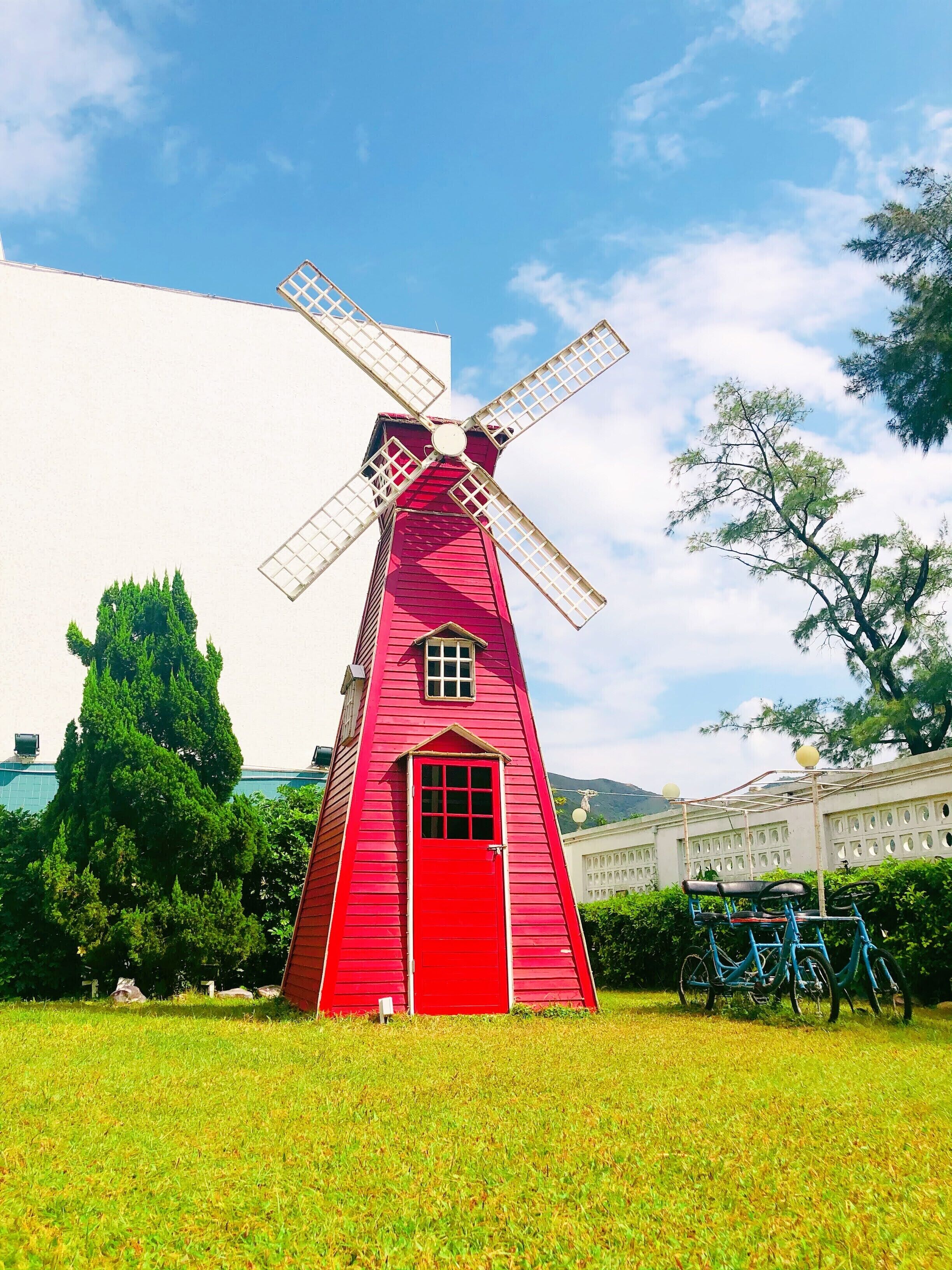 A red windmill with a white base, surrounded by green grass and trees.