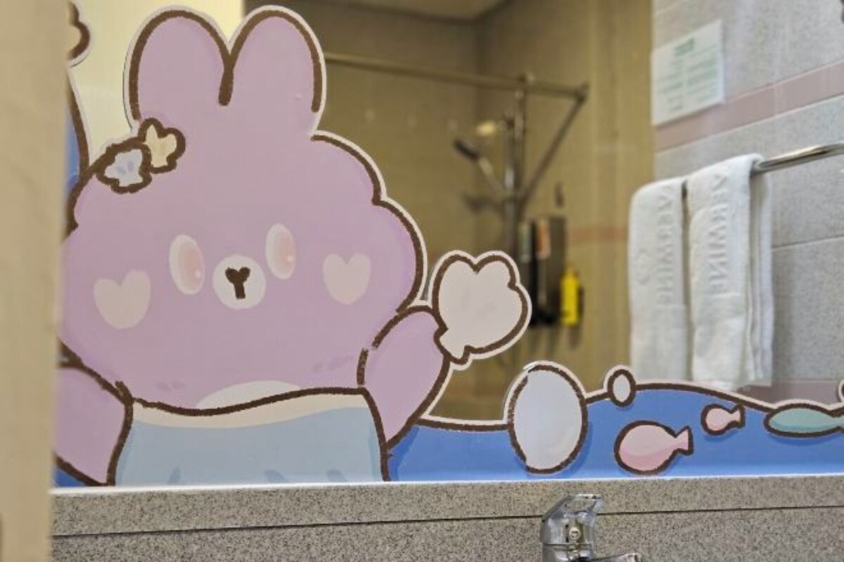 A bathroom with a large mirror, a towel rack, and a decorative cutout of a cartoon character.