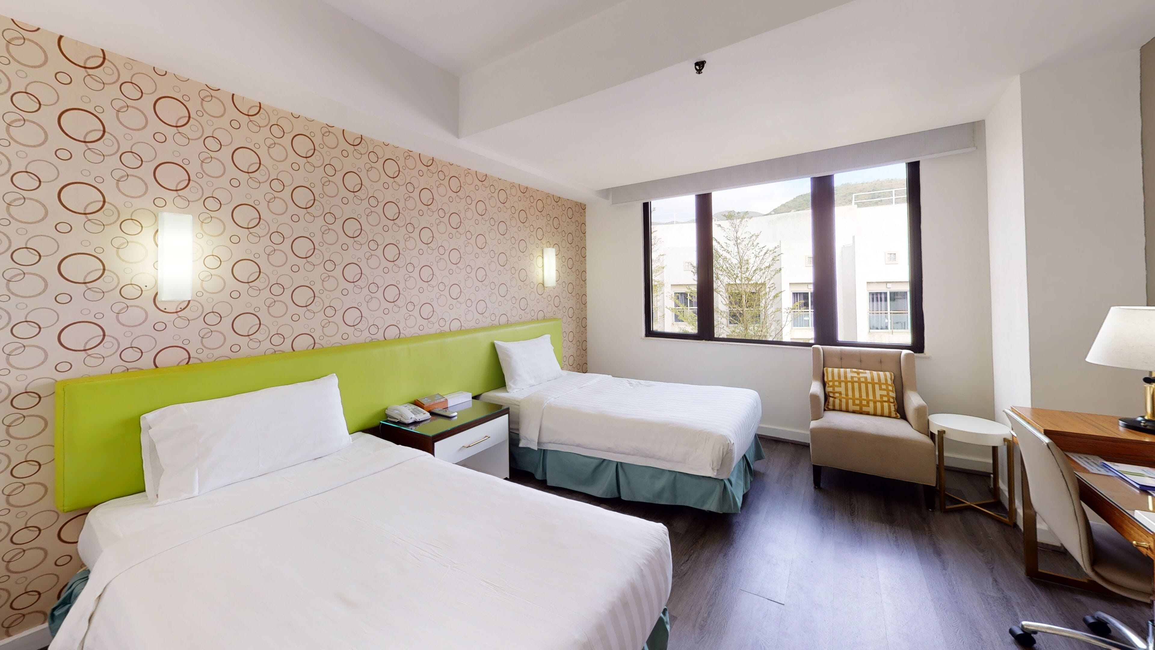 A hotel room with two beds, a desk, a chair, and a window with a view.