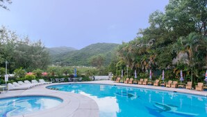 A swimming pool with lounge chairs and umbrellas, surrounded by greenery and hills. - Silvermine Beach Resort (Mui Wo)