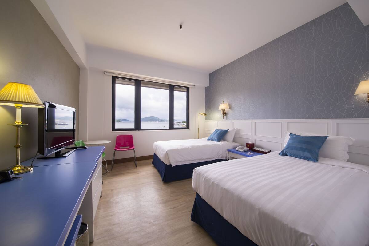 Una habitación de hotel con dos camas, un escritorio con computadora, una silla y una ventana con vistas.