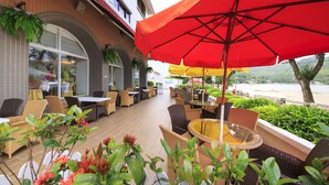 An outdoor patio area with wicker furniture, red and yellow umbrellas, and potted plants. - Silvermine Beach Resort (Mui Wo)