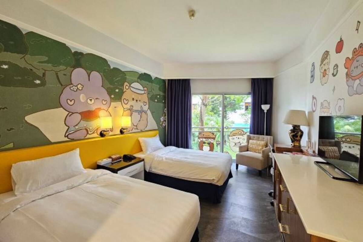 A hotel room with two beds, a desk, and a large window.
