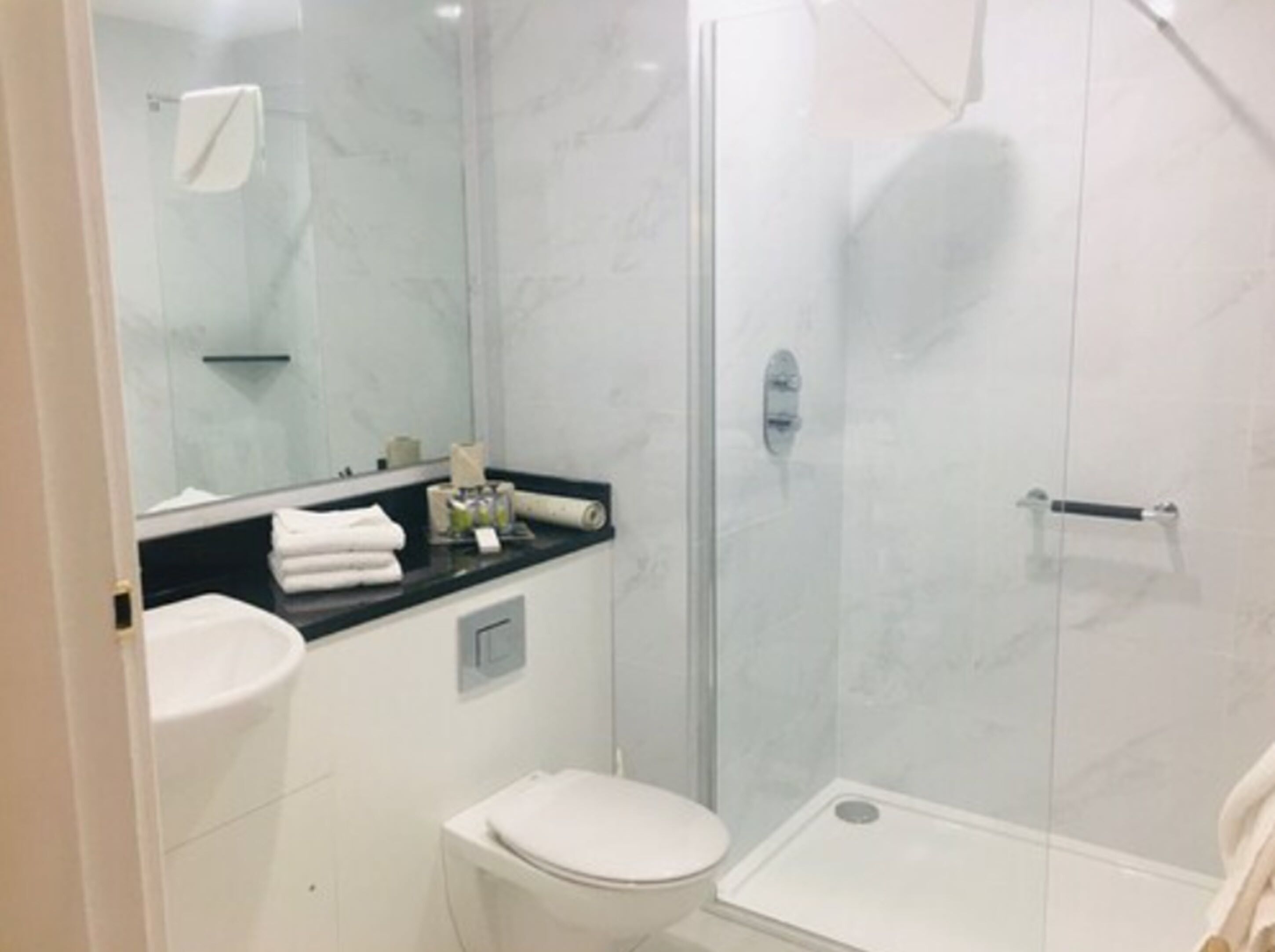 A modern bathroom with a glass shower enclosure, a white toilet, and a sink with a black countertop.