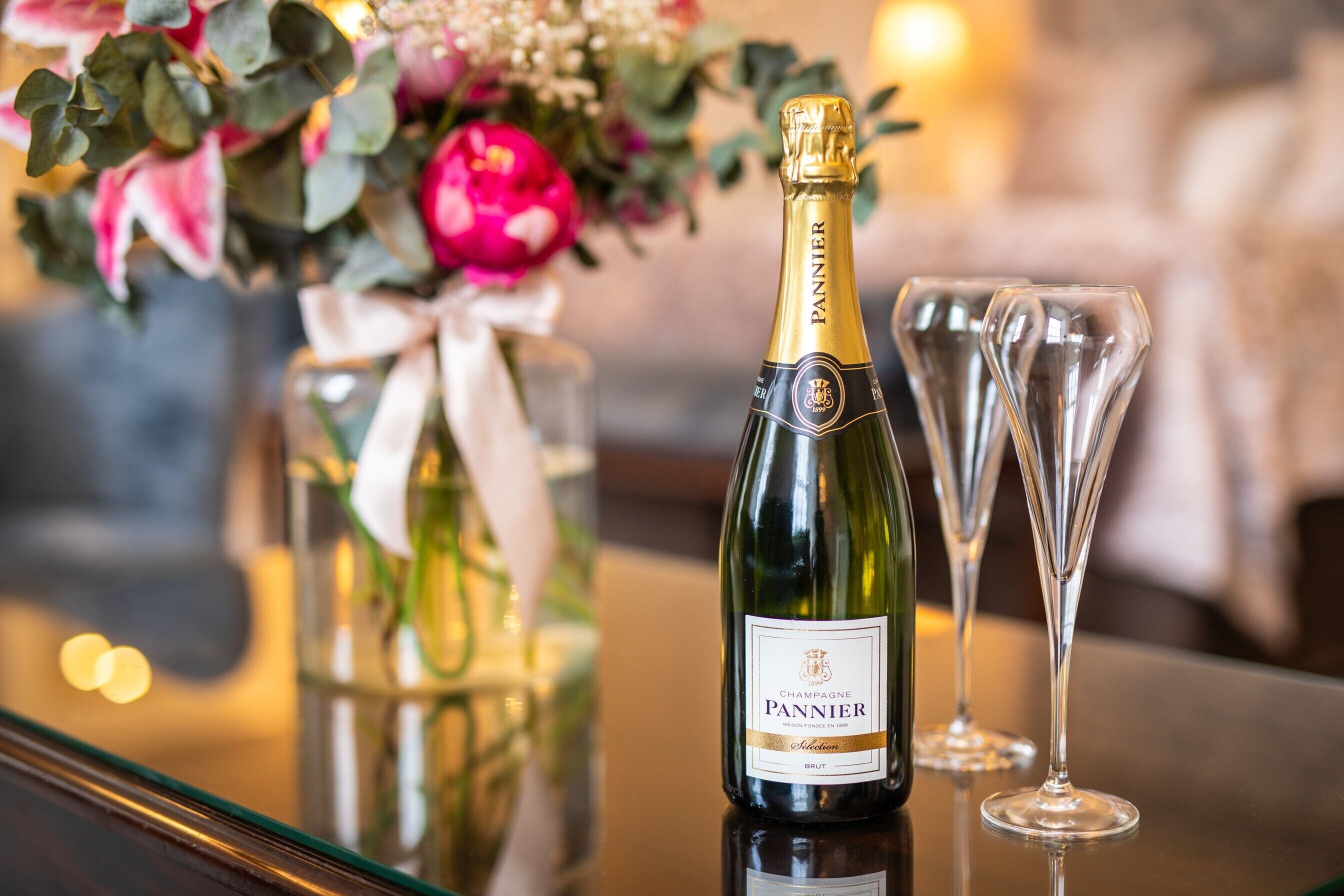 A bottle of Pannier champagne and two glasses on a reflective surface.