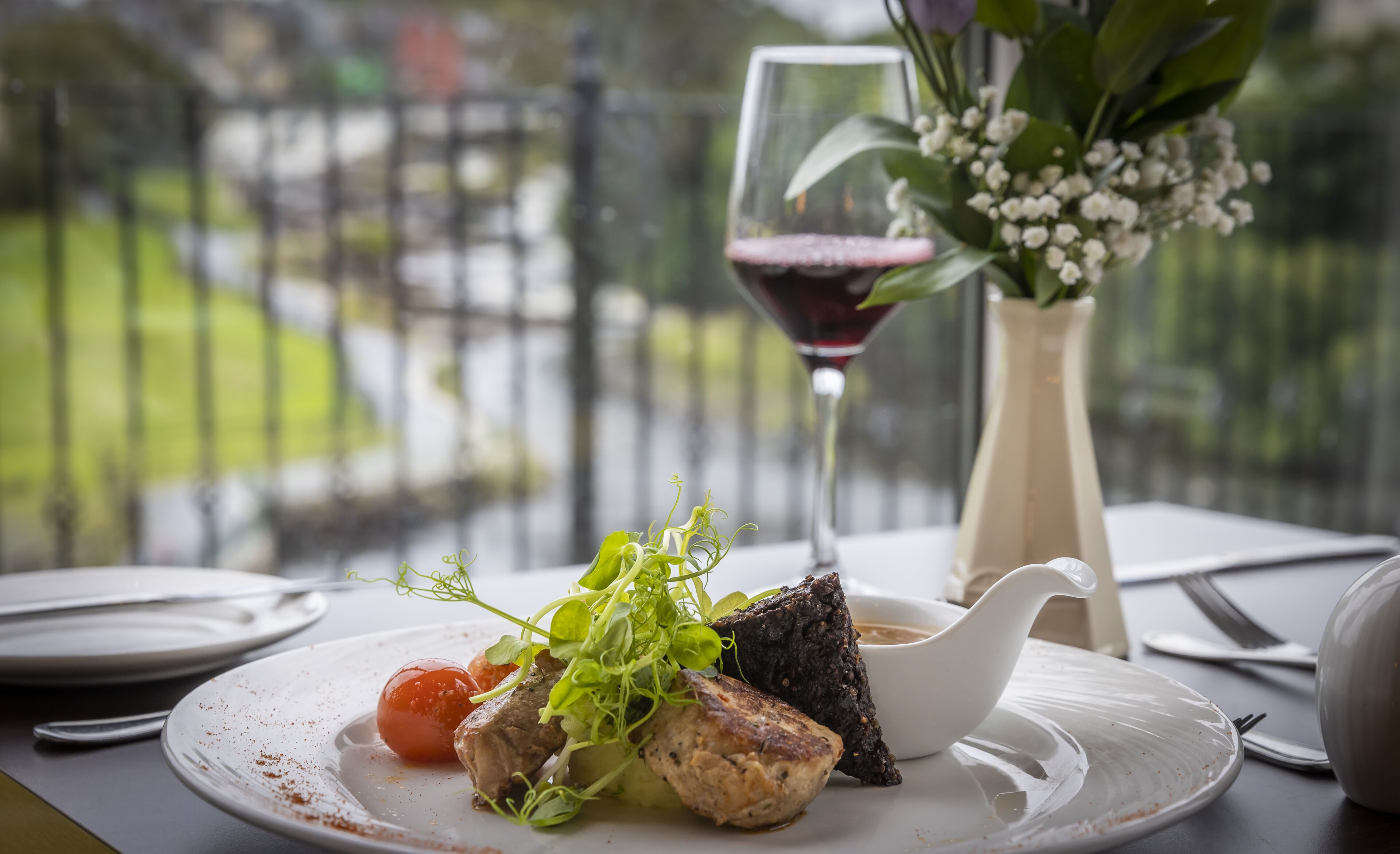 A dining table with plates of food, a glass of red wine, and a vase of flowers.