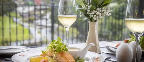 Una mesa de comedor con un plato de comida, dos copas de vino blanco y un florero con flores.