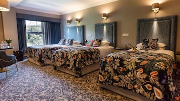 Habitación de hotel con dos camas, cada una con ropa de cama floral, un ventanal con cortinas y lámparas de pared.