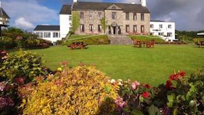 A large stone building with a symmetrical facade, a central entrance, and a well-maintained lawn with flower beds. - Falls Hotel & Spa (Ennistimon)