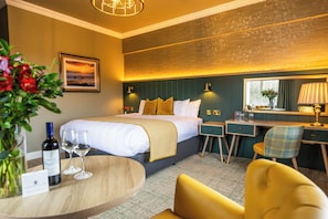 A hotel room with a bed, bedside tables, a desk, a chair, a mirror, and a vase with flowers. - Falls Hotel & Spa (Ennistimon)