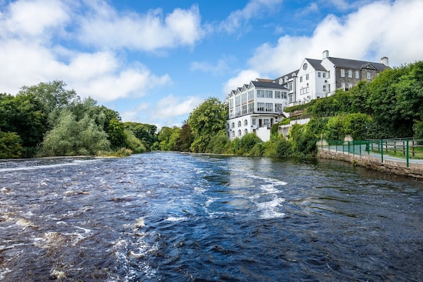 A river with a building on the right bank, surrounded by greenery. - Falls Hotel & Spa (Ennistimon)
