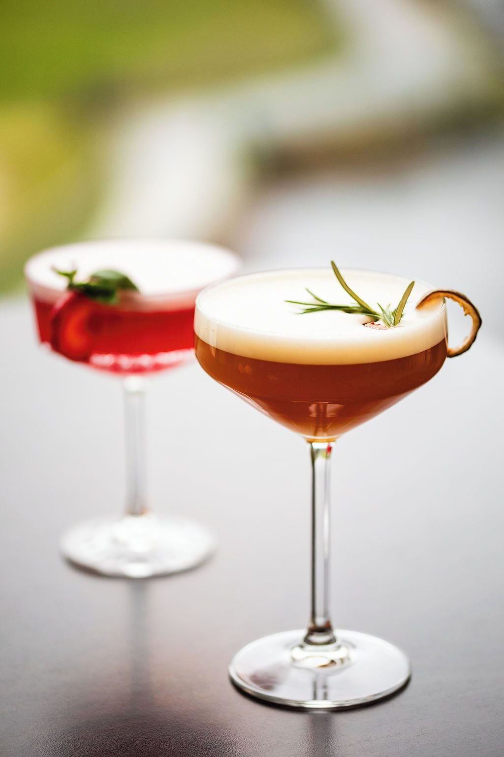 Two martini glasses on a reflective surface with a blurred background.