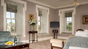 A hotel room with a bed, a sofa, a television, a table with a bottle and glasses, and a window with a view. - Falls Hotel & Spa (Ennistimon)