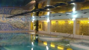 An indoor swimming pool with clear water, surrounded by walls with a textured design and warm lighting. - Falls Hotel & Spa (Ennistimon)