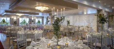 Un salón de banquetes con mesas redondas, candelabros y cortinas blancas.