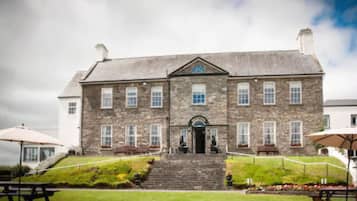 A large stone building with a central entrance, multiple windows, and a small garden area with steps leading up to the entrance.