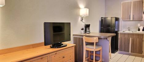 Cocina compacta con encimera de madera, refrigerador negro, cafetera y televisor montado en la pared.
