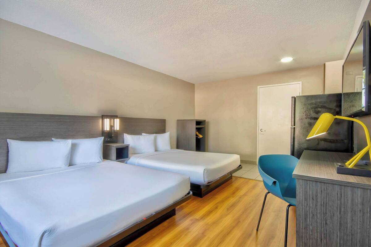 Habitación de hotel con dos camas, un escritorio con silla, un espejo y un armario.