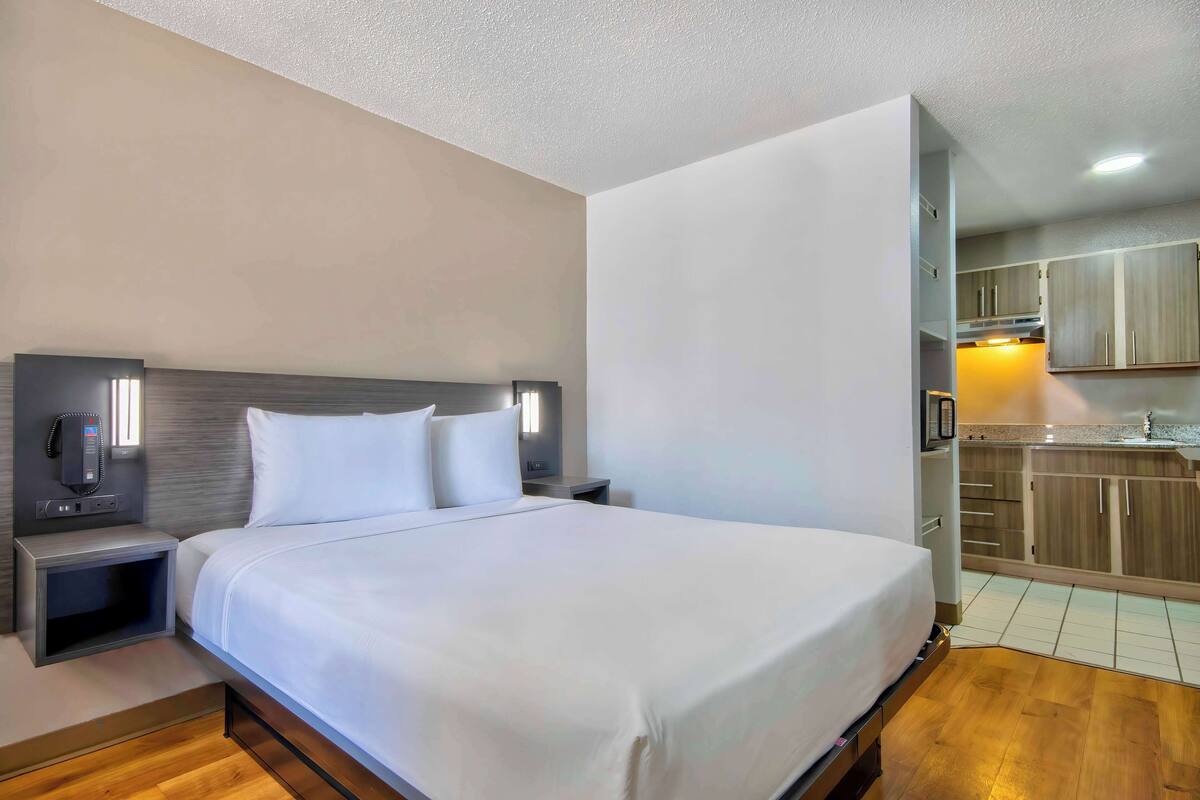 Una habitación de hotel con una cama grande, mesitas de noche, televisión integrada y una zona de kitchenette.