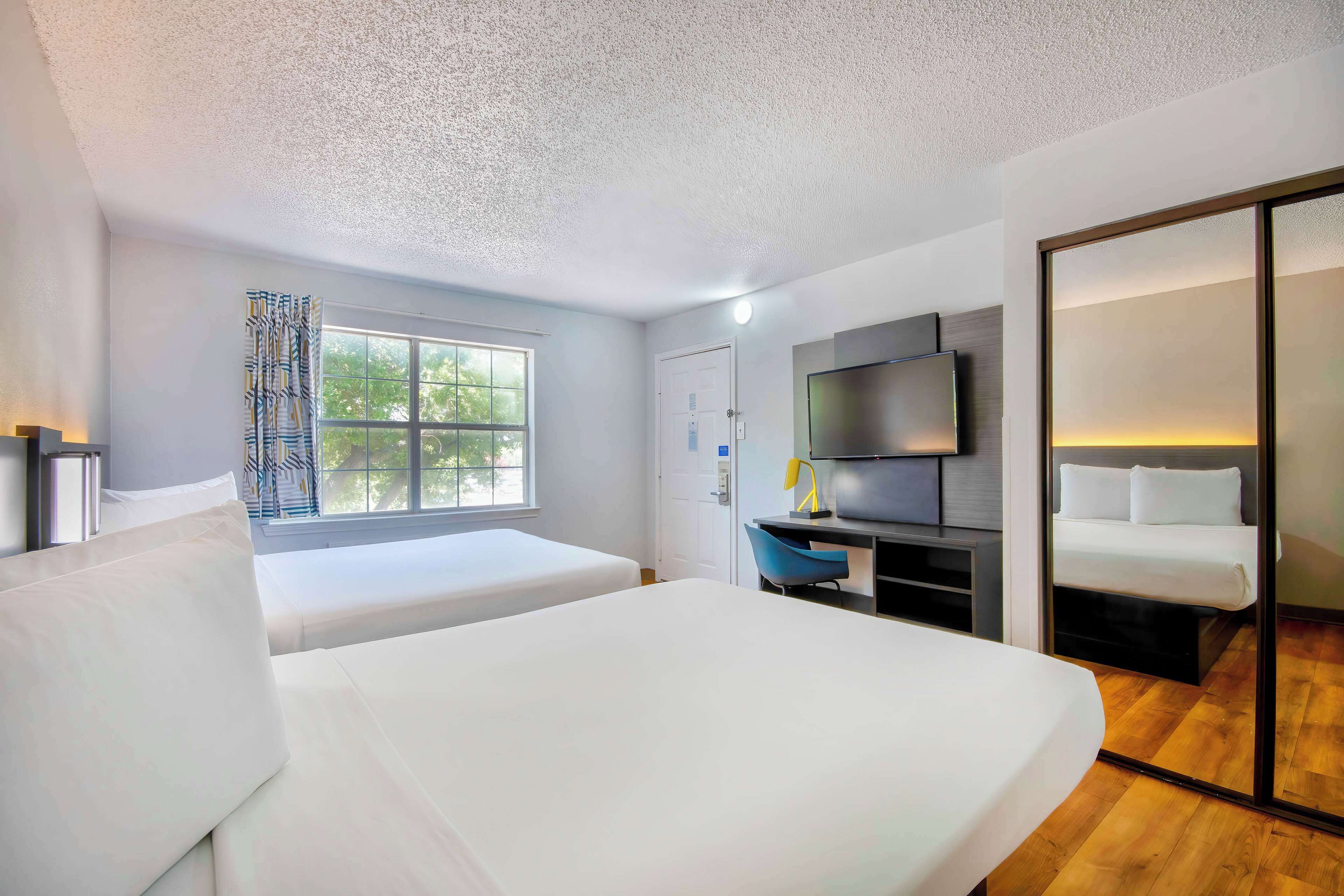 A hotel room with two beds, a desk with a chair, a TV, and a sliding door closet.