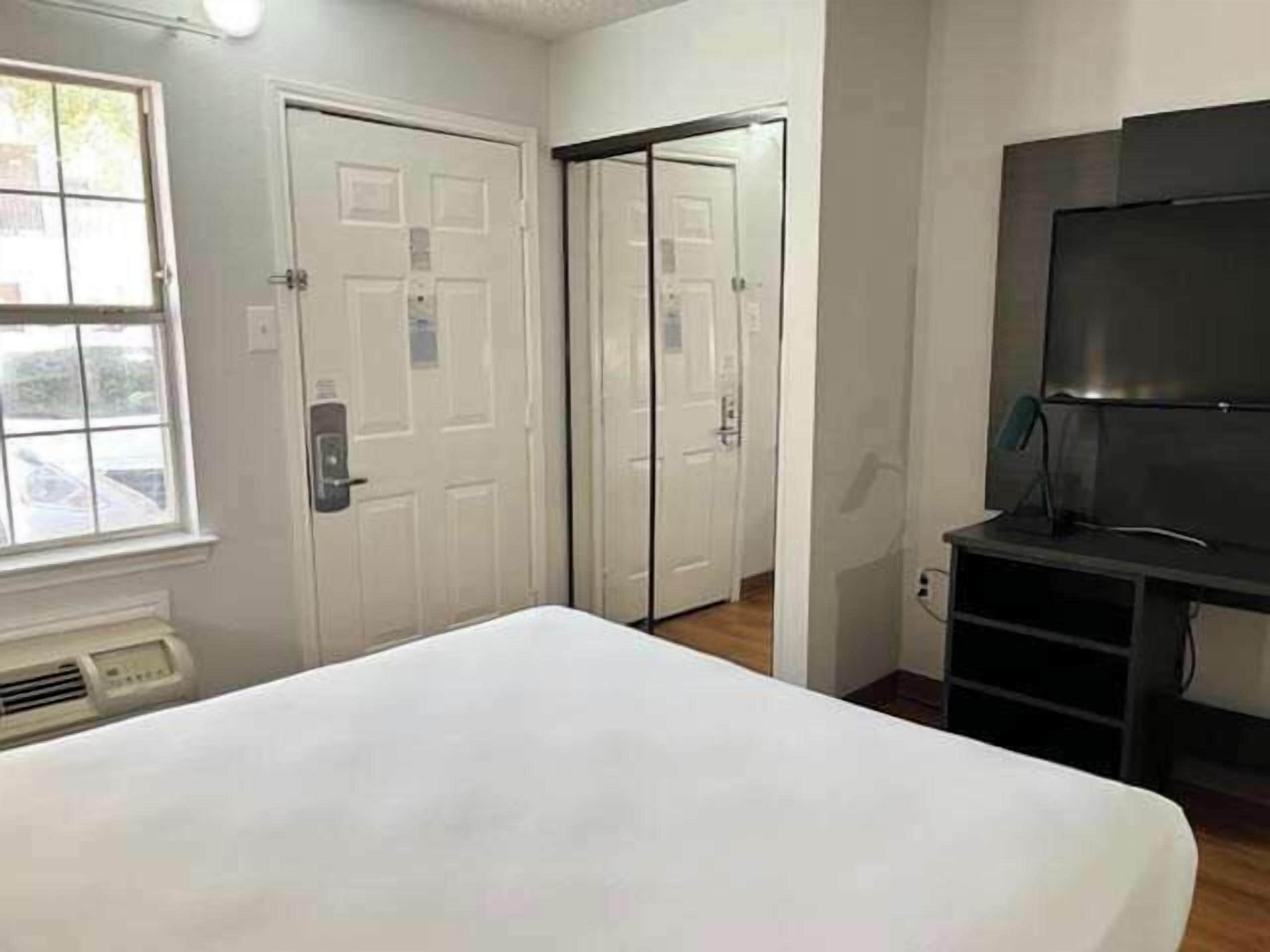 A hotel room with a bed, a television, a window, and a door.