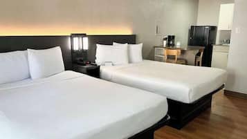 A hotel room with two beds, a desk with a chair, a television, and a kitchenette.