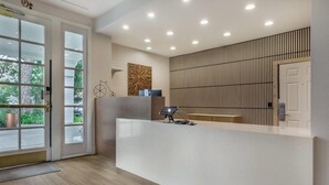A reception area with a white reception desk, a wooden panel wall, and a door with a glass panel. - University Park Inn & Suites, an Ascend Collection Hotel (Davis)