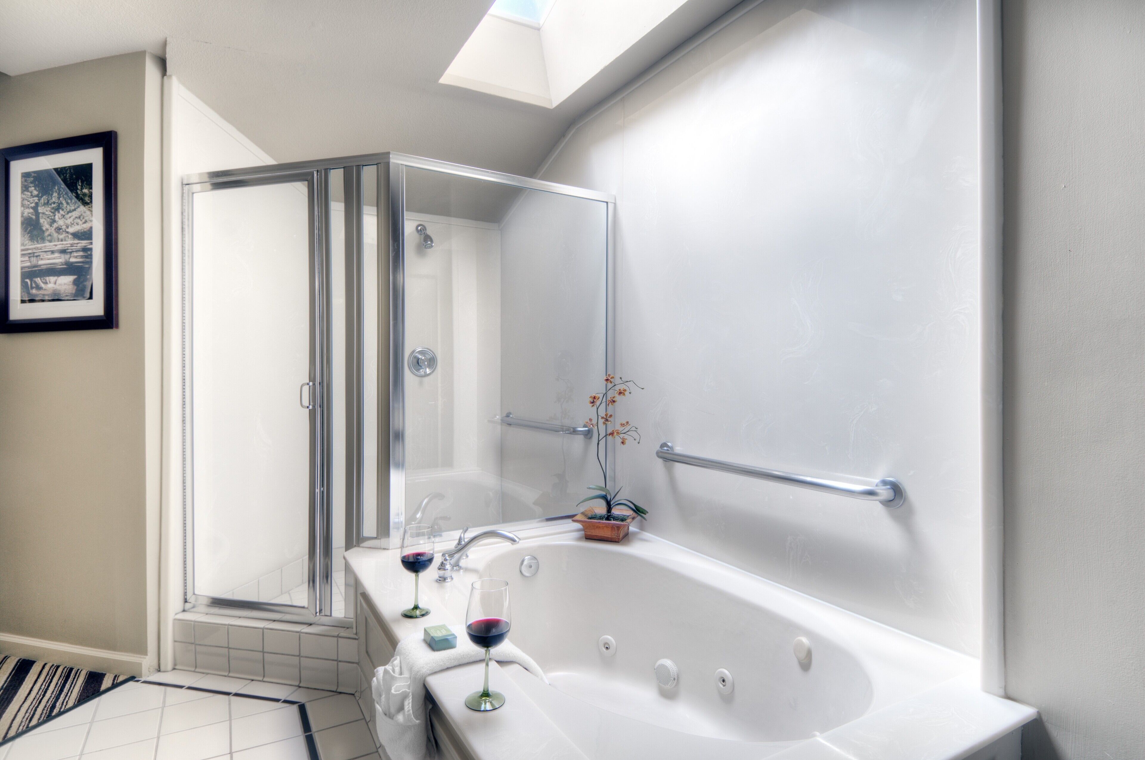 Une salle de bain moderne avec une douche à l’italienne, une baignoire dotée d’une porte en verre, et deux verres à vin posés sur le bord.