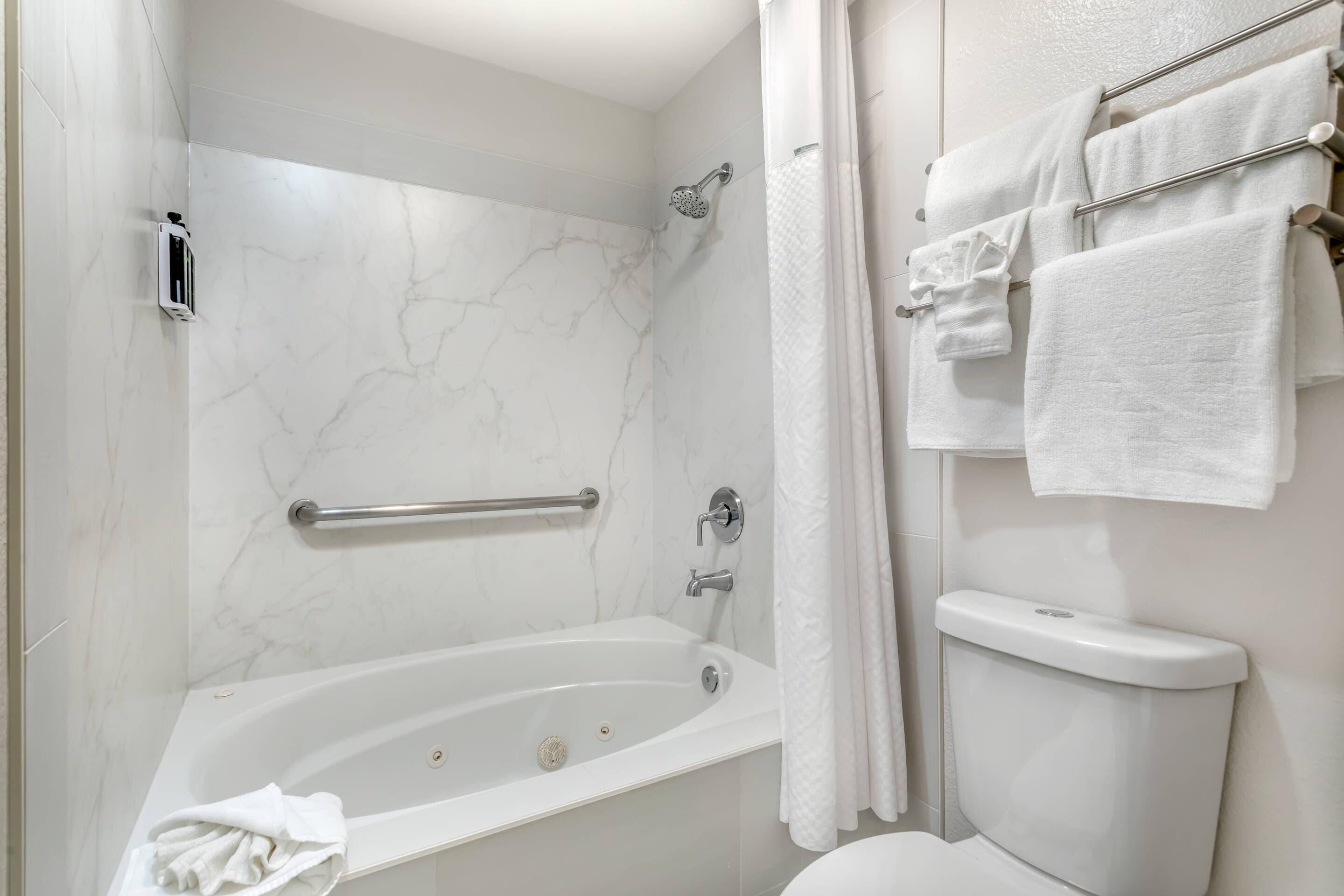 A modern bathroom with a marble wall, a bathtub, a toilet, and a towel rack with multiple towels.