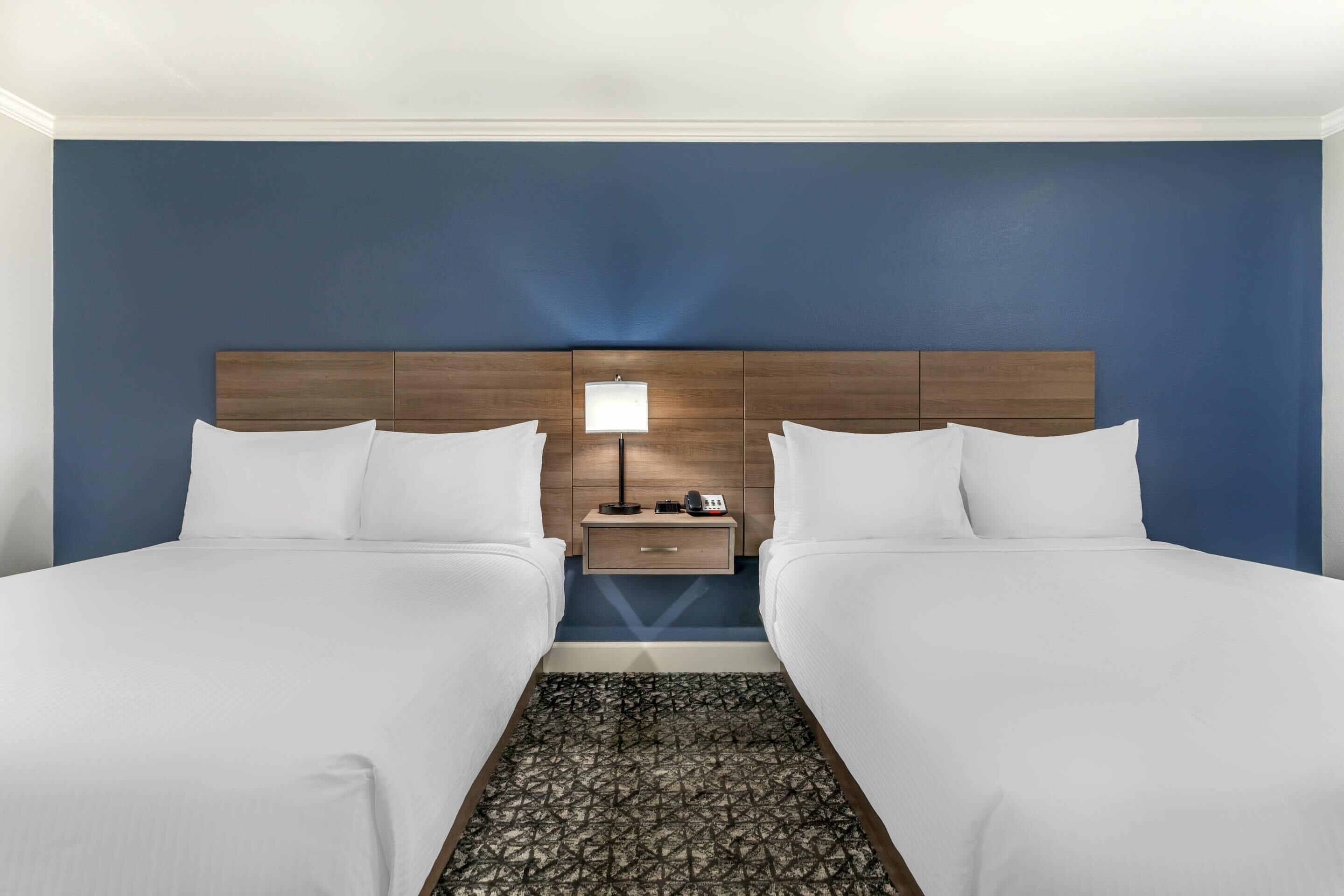 A hotel room with two beds, a nightstand with a lamp, and a patterned rug.