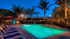A swimming pool with lounge chairs and umbrellas, surrounded by palm trees and well-lit pathways. - University Park Inn & Suites, an Ascend Collection Hotel (Davis)