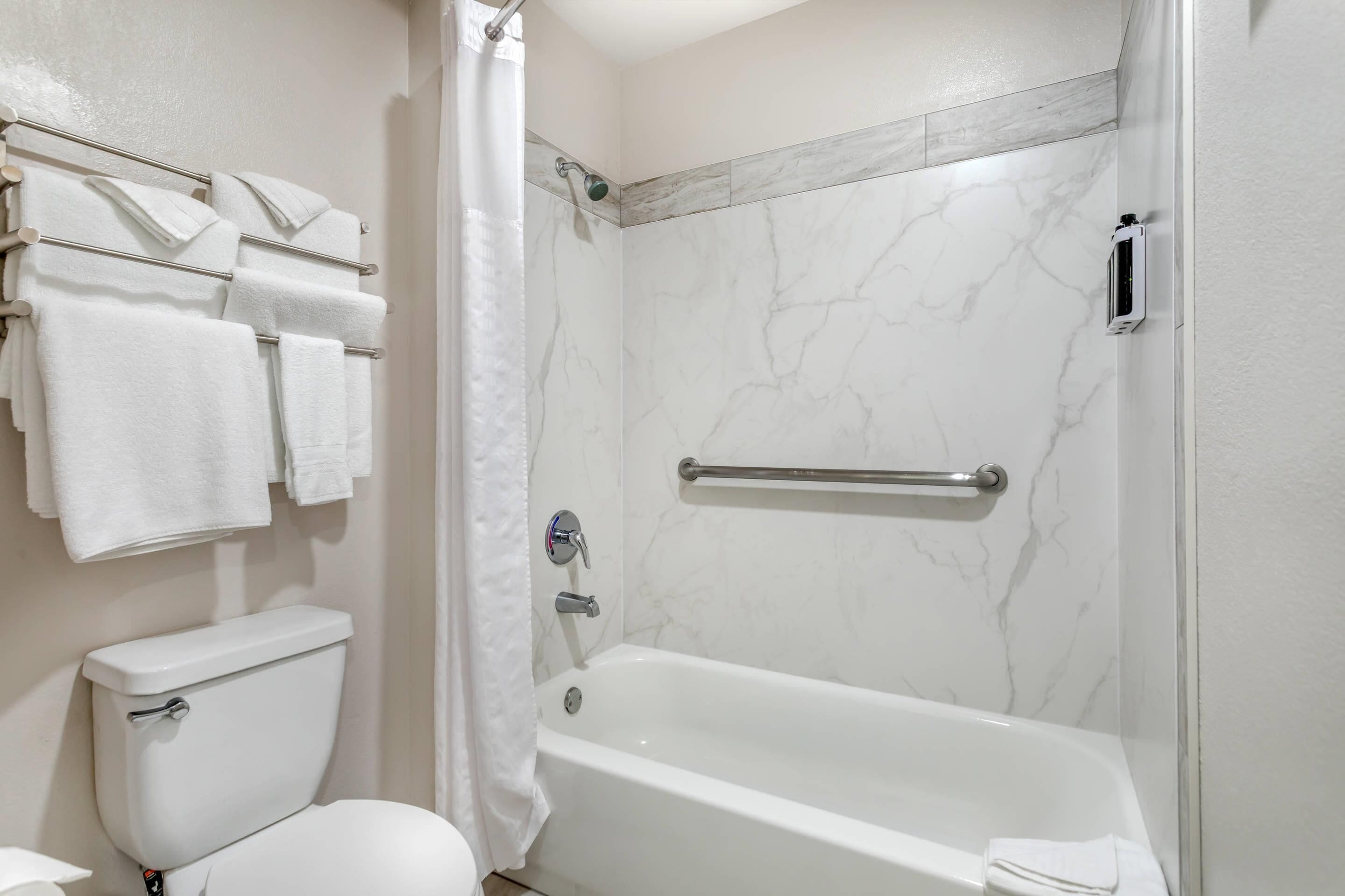A bathroom with a toilet, bathtub, towel rack, shower curtain, and marble walls.