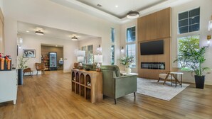 A spacious living area with a wooden floor, a green sofa, a coffee table, and a TV mounted on the wall. - University Park Inn & Suites, an Ascend Collection Hotel (Davis)