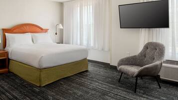 Quarto de hotel com uma cama grande, uma cadeira, televisão de tela plana e janela com cortinas.
