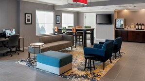 A modern hotel lobby with a sofa, ottoman, bar area, and a dining table with chairs. - TownePlace Suites by Marriott Wilmington Newark/Christiana (Newark)